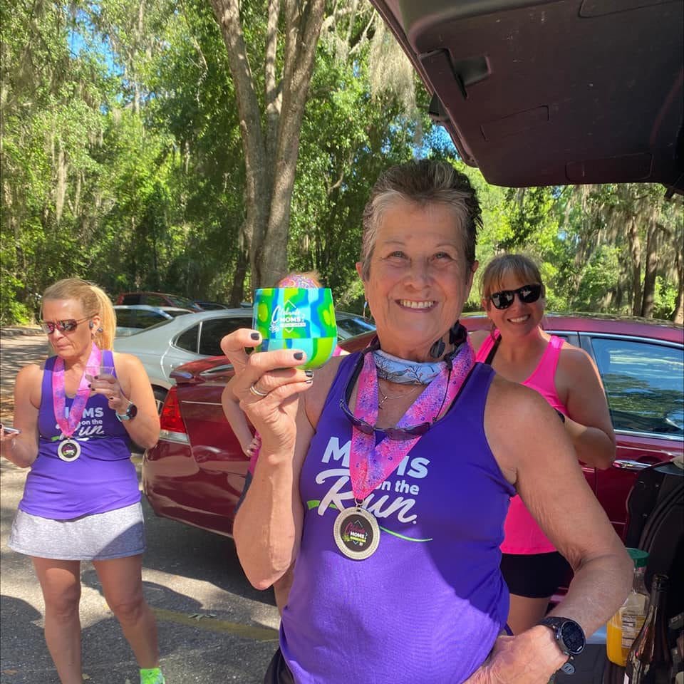 A Moms on the Run member wearing a purple race shirt, Celebrate Moms medal and holding a branded cup