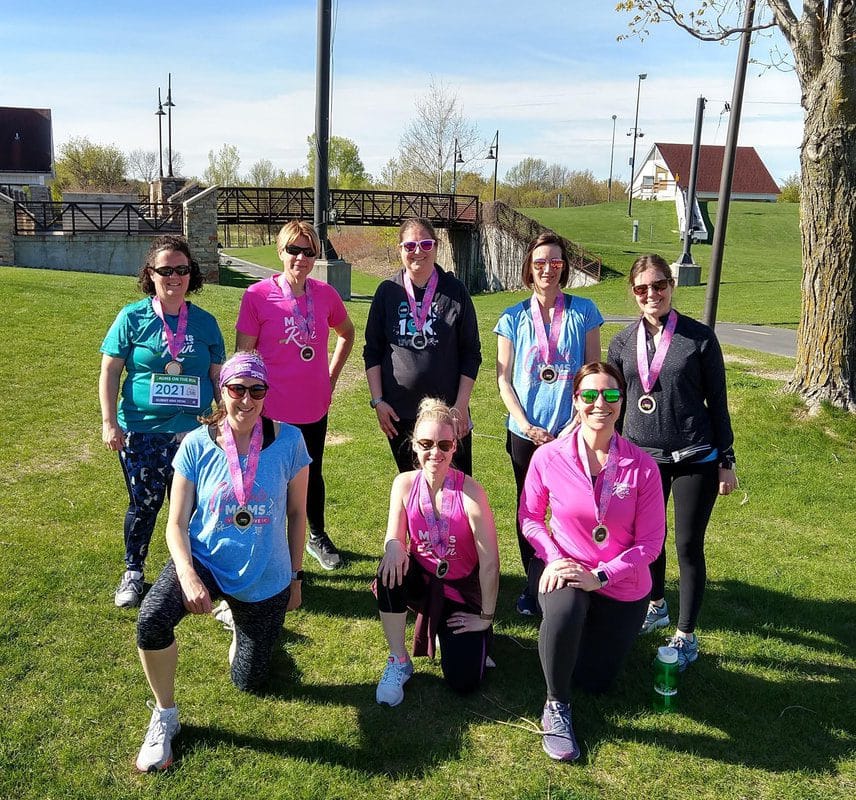 A group of Moms on the Run women standing on a grass wearing Celebrate Moms medals