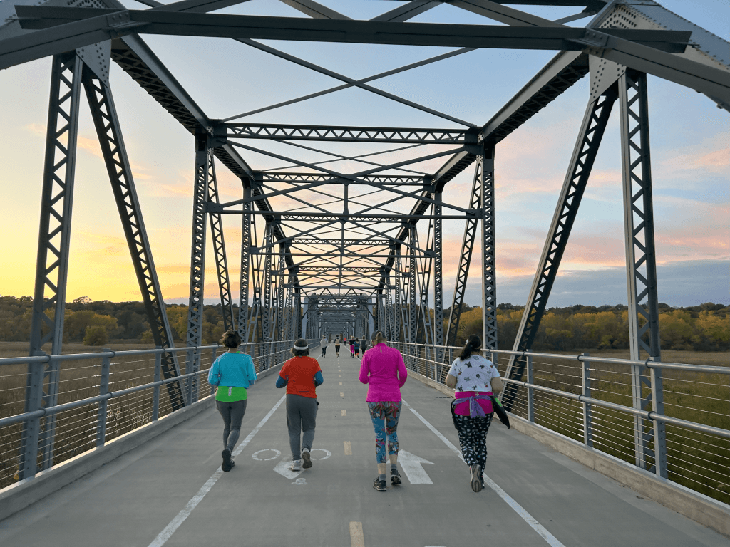 A group of runners jogging across a bridge at sunset with colorful leaves on the trees