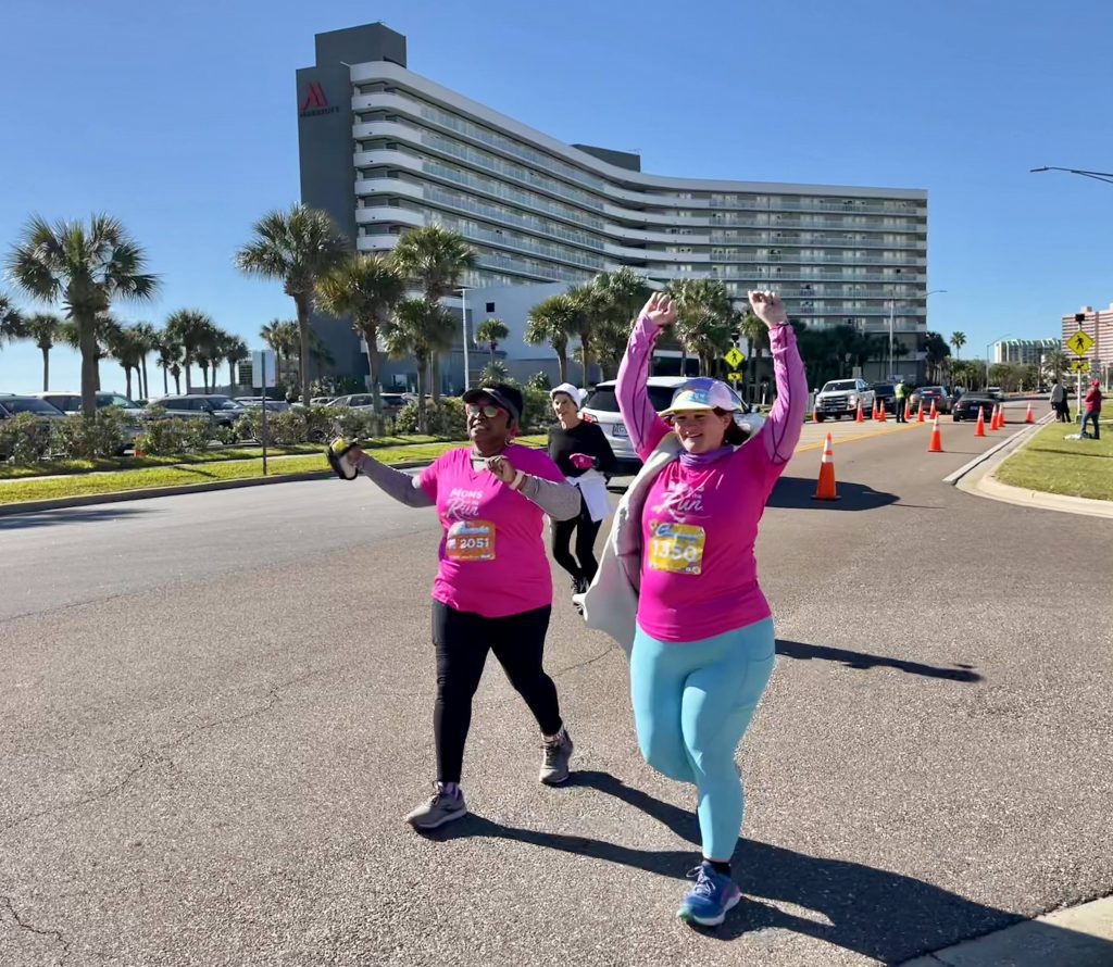 women running a half-marathon at the annual MOTR destination race. One women has her arms up in victory.