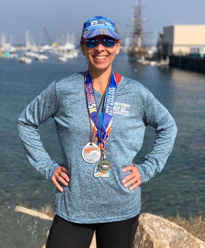 Coach Becky from shoreview standing triumphantly in front of a large body of water. She wears two medals.