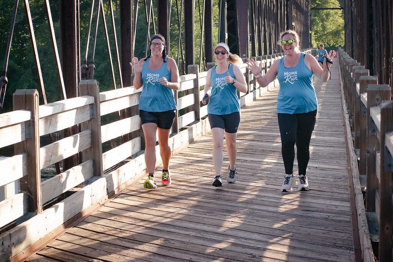 Three happy women running wearing blue Moms on the Run shirts