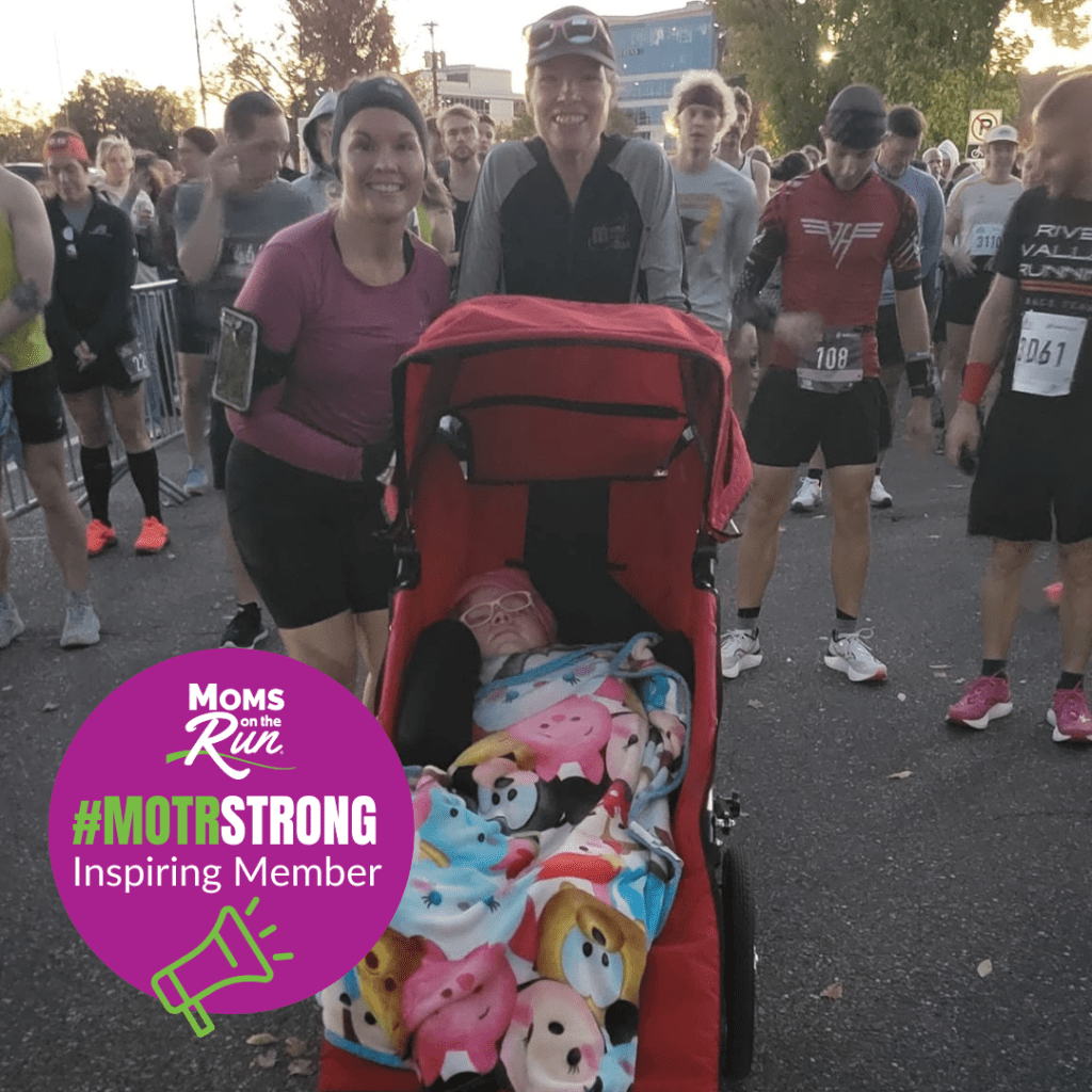 Two women standing and girl in jogging stroller at start of race