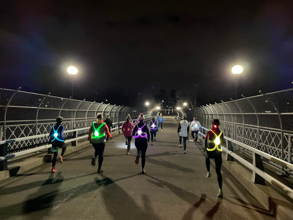 Moms on the Run members running on a bridge at night wearing reflective and light-up gear