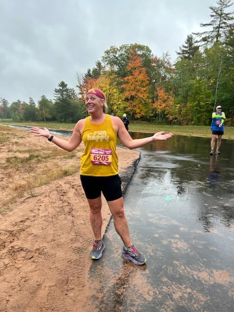 Coach and Owner of the Chanhassen and Chaska Locations, Kate, stands on a beach with a race bib on.