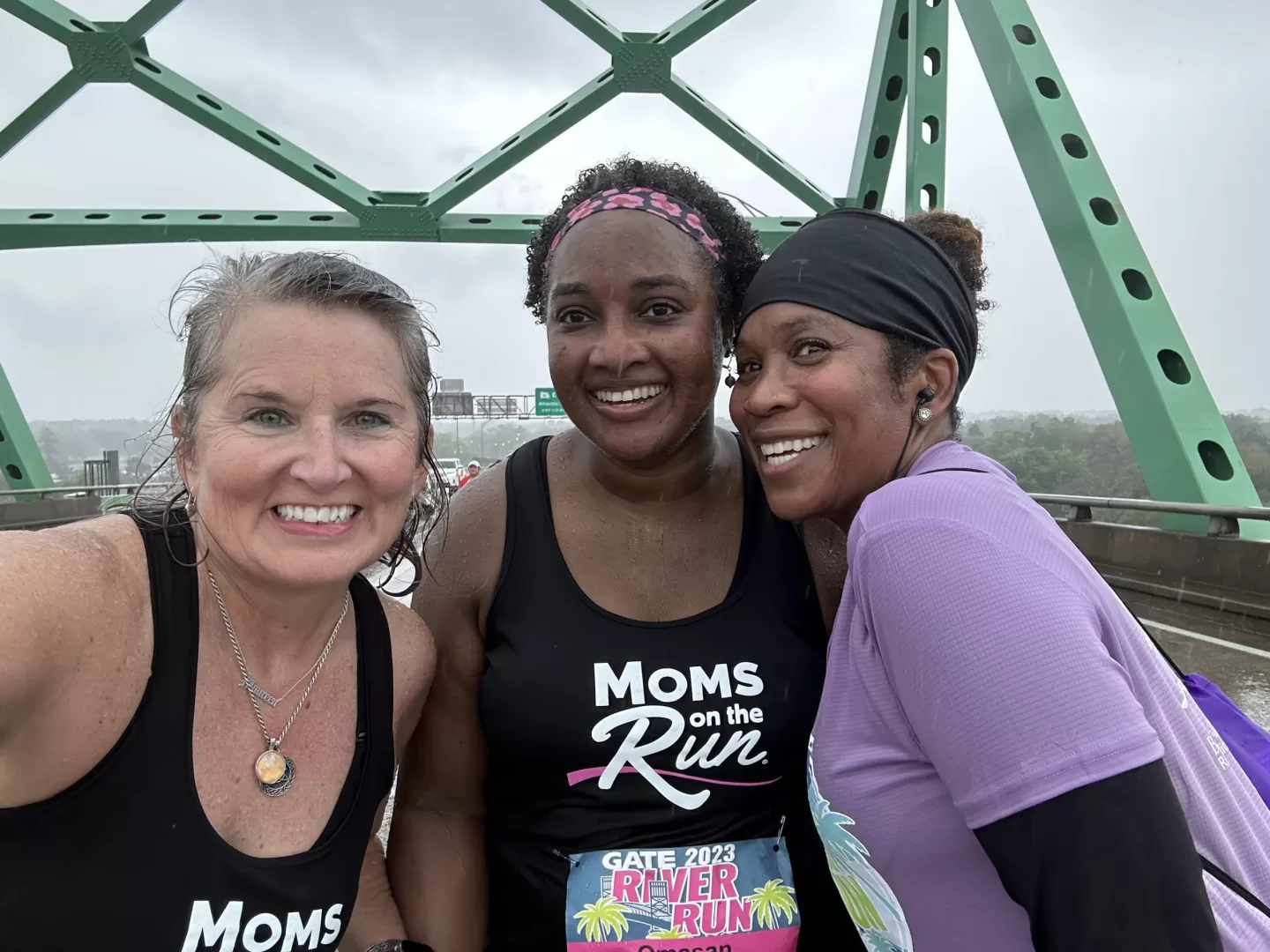 Three female runners smiling on a bridge
