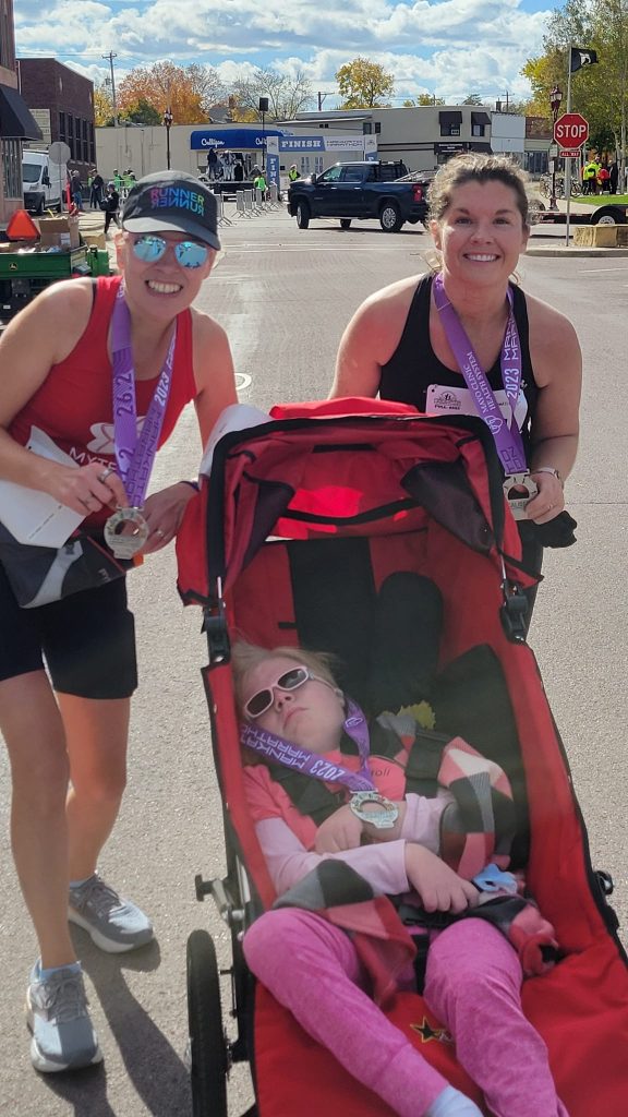 Two runners and girl in jogging stroller smiling at finish line