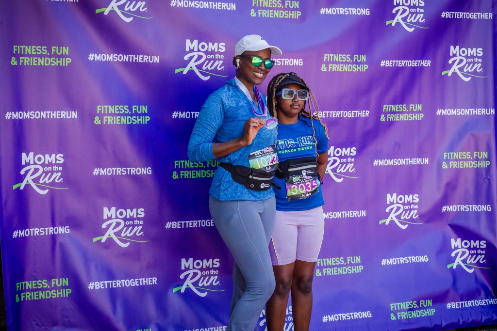 Mother and daughter wearing race bibs and posing in front of a MOTR background banner