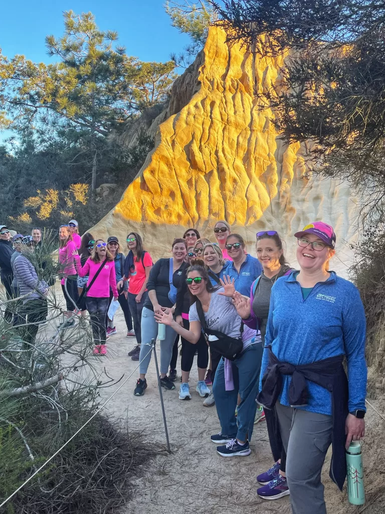 A large group of MOTR members on a destination trip. They're standing by a large rock waving.