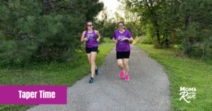 two female runners in purple shirts running on pavement trail